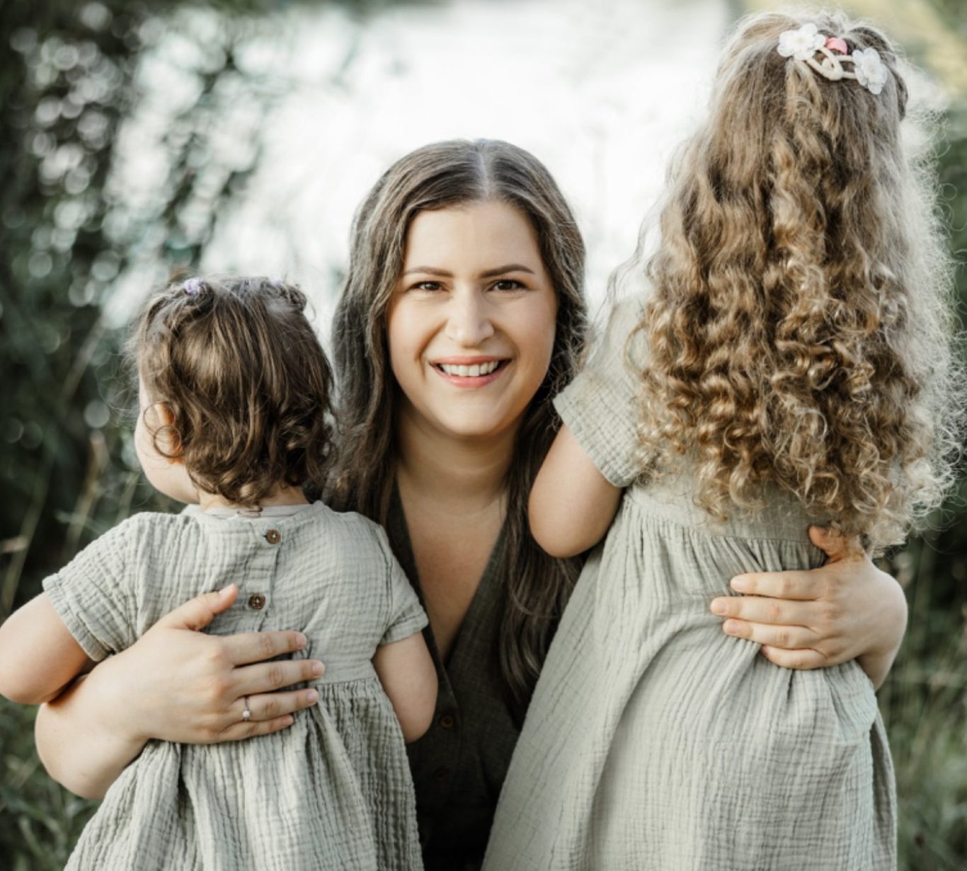 Still-, Schlaf- und Beikostberaterin aus Straubing-Bogen lächelt in die Kamera, hält ihre beiden Kinder im Arm, die nur von hinten zu sehen 